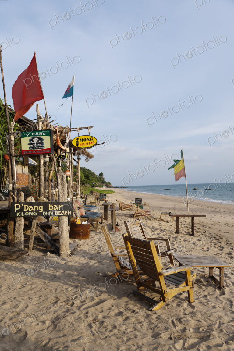 Beach bar and cabins on a sandy beach, with flags and furniture, on the Andaman coast.