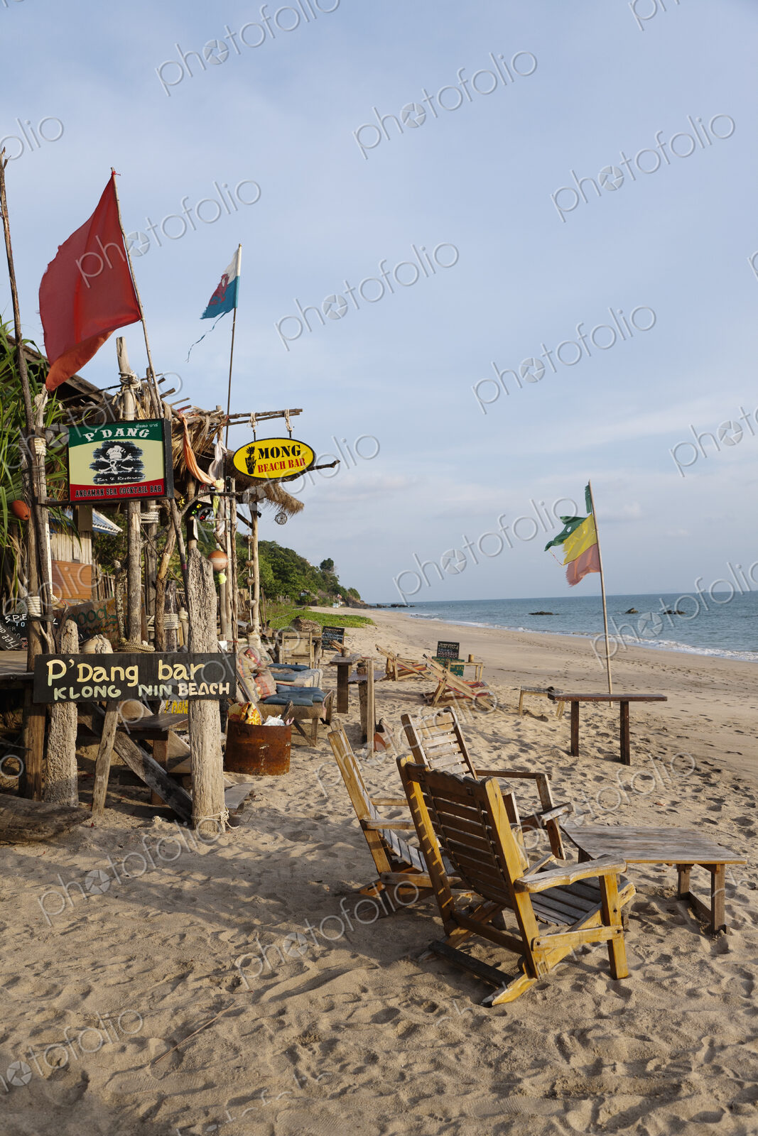 Beach bar and cabins on a sandy beach, with flags and furniture, on the Andaman coast.