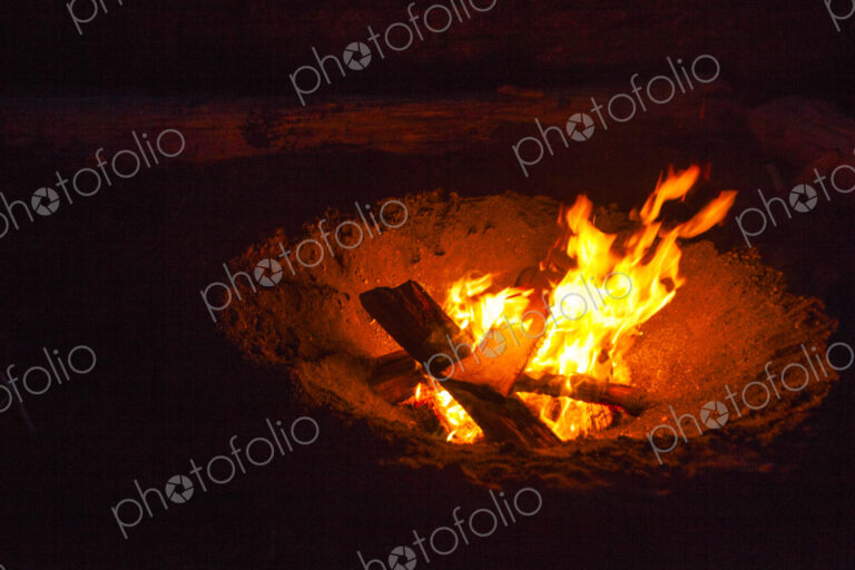 Beach fire along Puget Sound at night, glowing embers and flames rising.