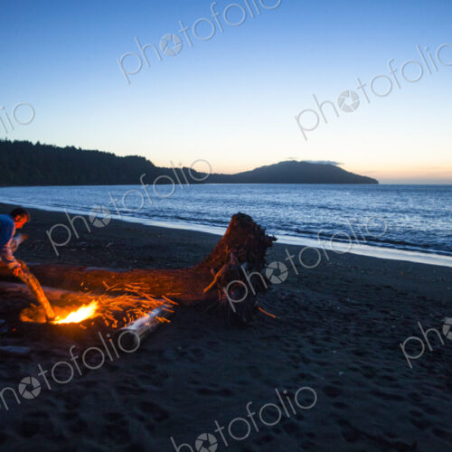 Beach fire on Puget Sound, glowing embers of logs at dusk.