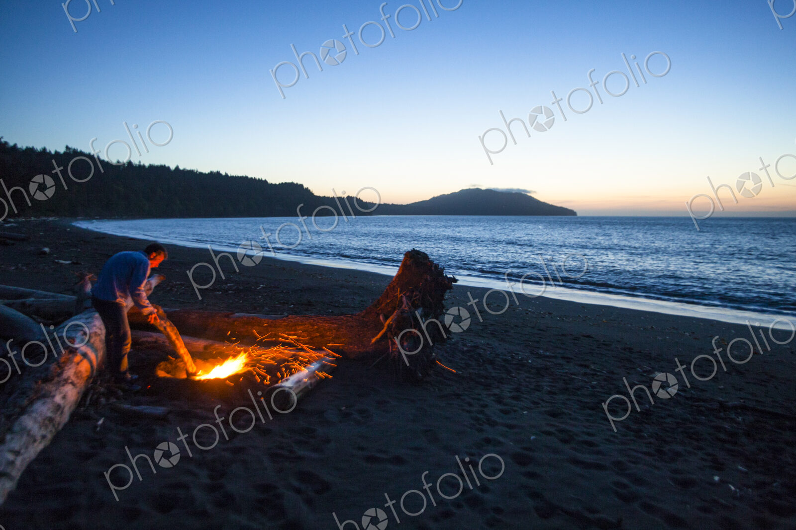 Beach fire on Puget Sound, glowing embers of logs at dusk.