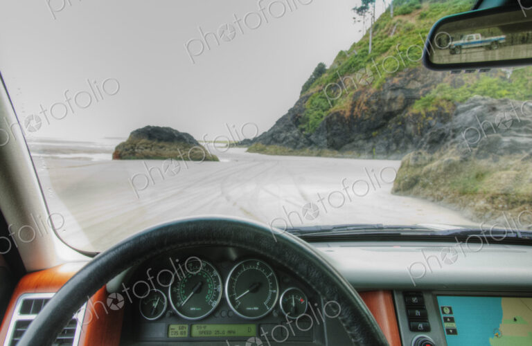 Beach seen from driver's seat of a car, with steering wheel in foreground.