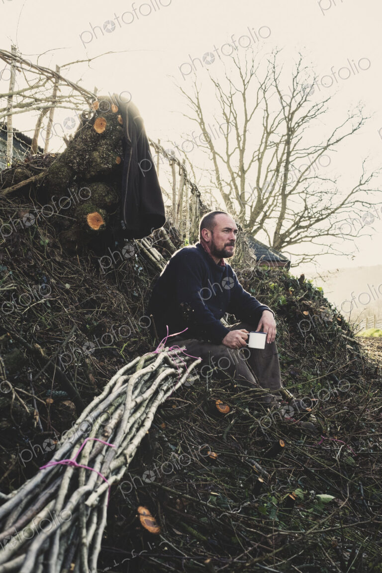 Bearded man sitting on ground next to bunch of wooden pleachers used in traditional…