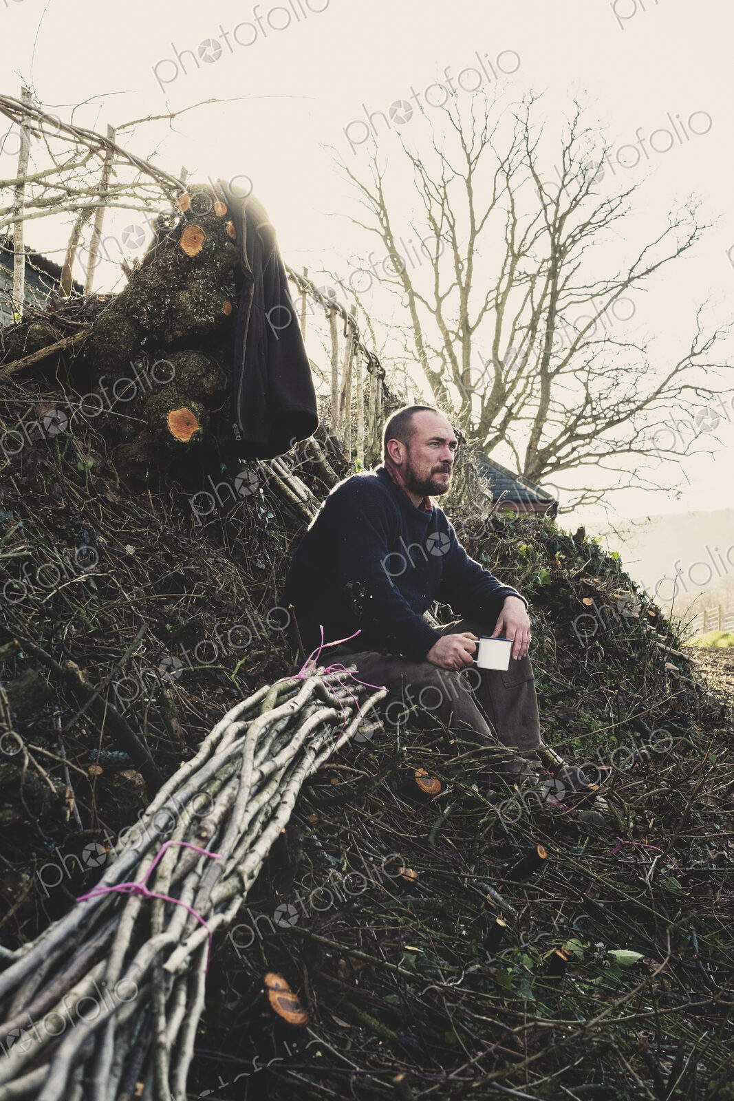 Bearded man sitting on ground next to bunch of wooden pleachers used in traditional…