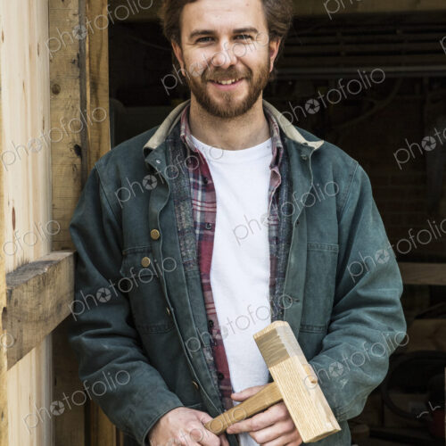 Bearded man standing in doorway of woodworking workshop, holding wooden mallet,… Bearded man standing in doorway of woodworking workshop, holding wooden mallet,…