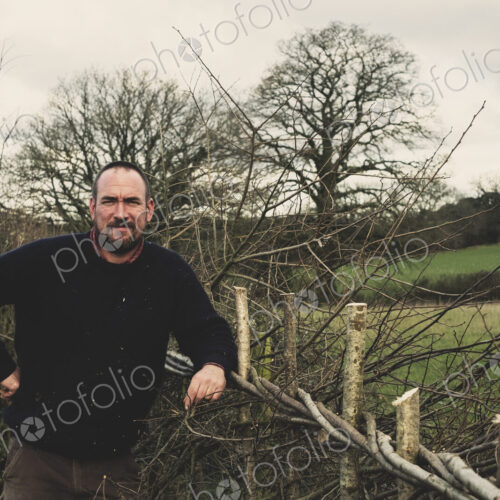 Bearded man standing next to a newly built traditional hedge, smiling at camera. Bearded man standing next to a newly built traditional hedge, smiling at camera.