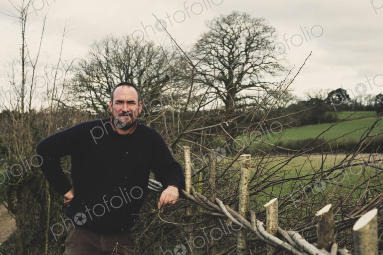 Bearded man standing next to a newly built traditional hedge, smiling at camera.