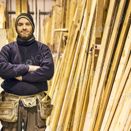 Bearded man wearing beanie and tool belt standing with his arms crossed next to a… Bearded man wearing beanie and tool belt standing with his arms crossed next to a…