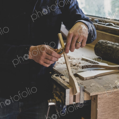 Bearded man wearing black beanie standing at workbench in workshop, working on piece… Bearded man wearing black beanie standing at workbench in workshop, working on piece…