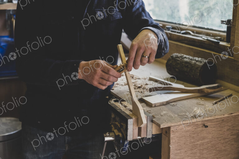 Bearded man wearing black beanie standing at workbench in workshop, working on piece…