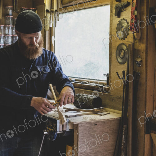 Bearded man wearing black beanie standing at workbench in workshop, working on piece… Bearded man wearing black beanie standing at workbench in workshop, working on piece…