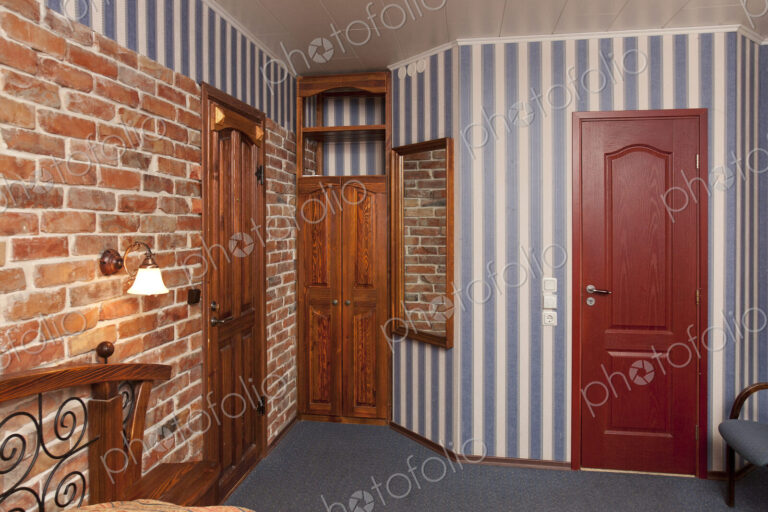 Bed in bedroom with wallpaper and brick wall and wooden cupboards and doors.