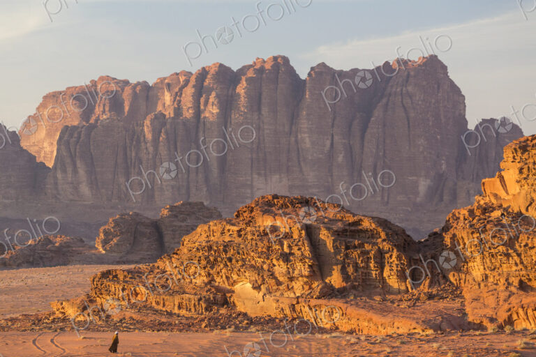 Bedouin walking through desert landscape with rocks and mountains.