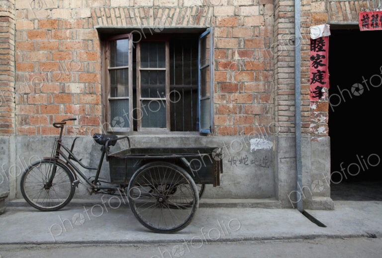 Bicycle and cart outside a small house on a street
