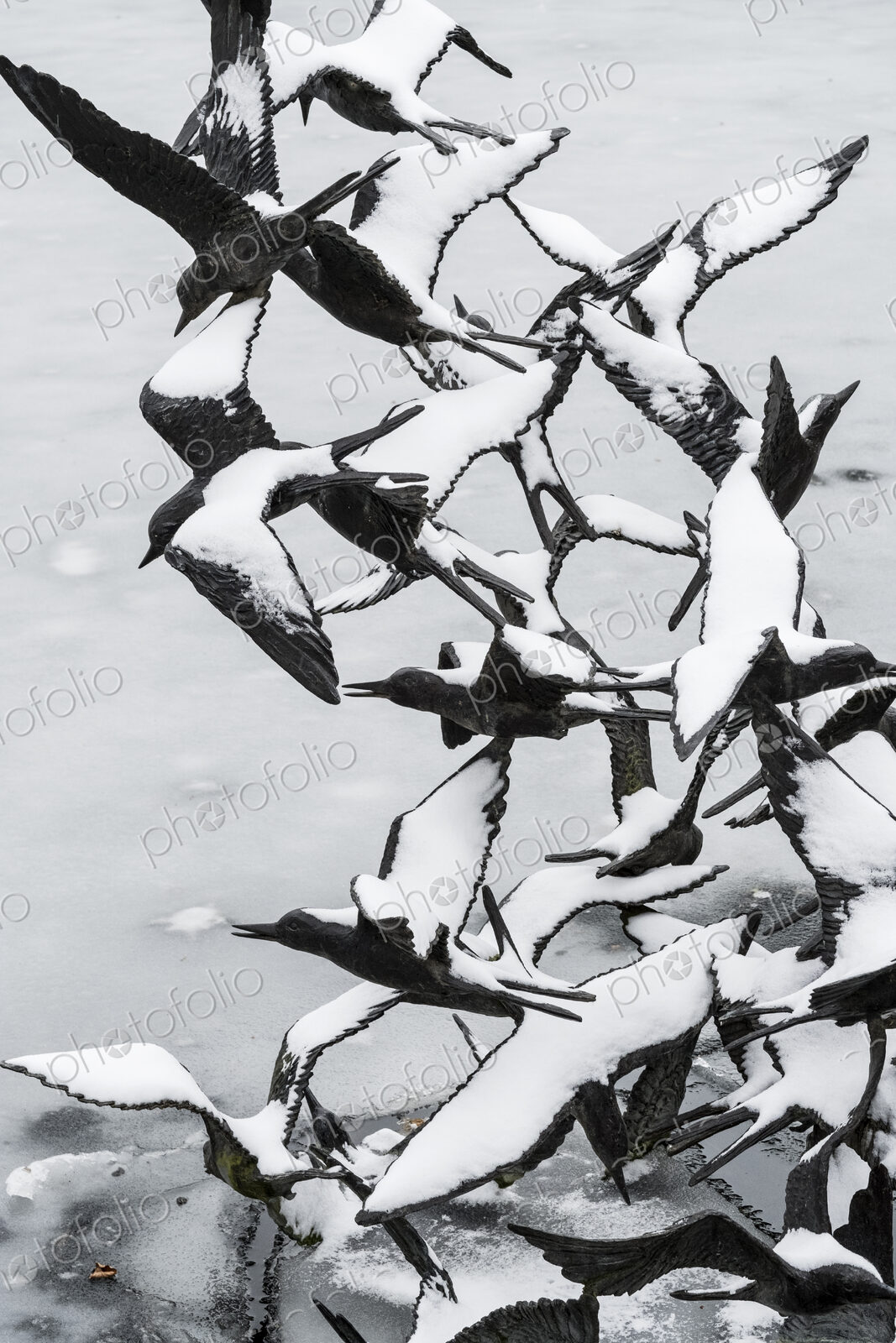 Bird sculpture, rising birds with snow covered outstretched wings, in winter above water.