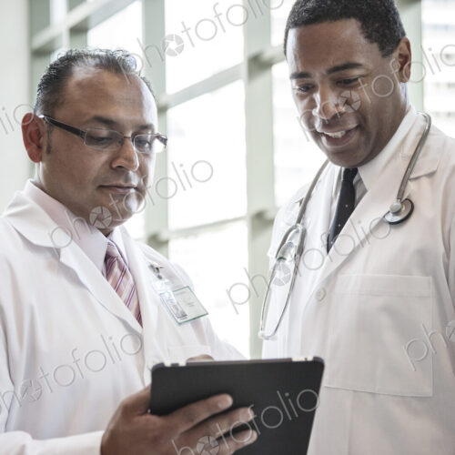 Black and Hispanic male doctors discussing a case in a hospital hallway. Black and Hispanic male doctors discussing a case in a hospital hallway.