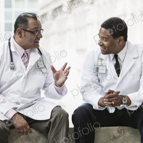 Black and Hispanic male doctors discussing a case in a hospital hallway. Black and Hispanic male doctors discussing a case in a hospital hallway.