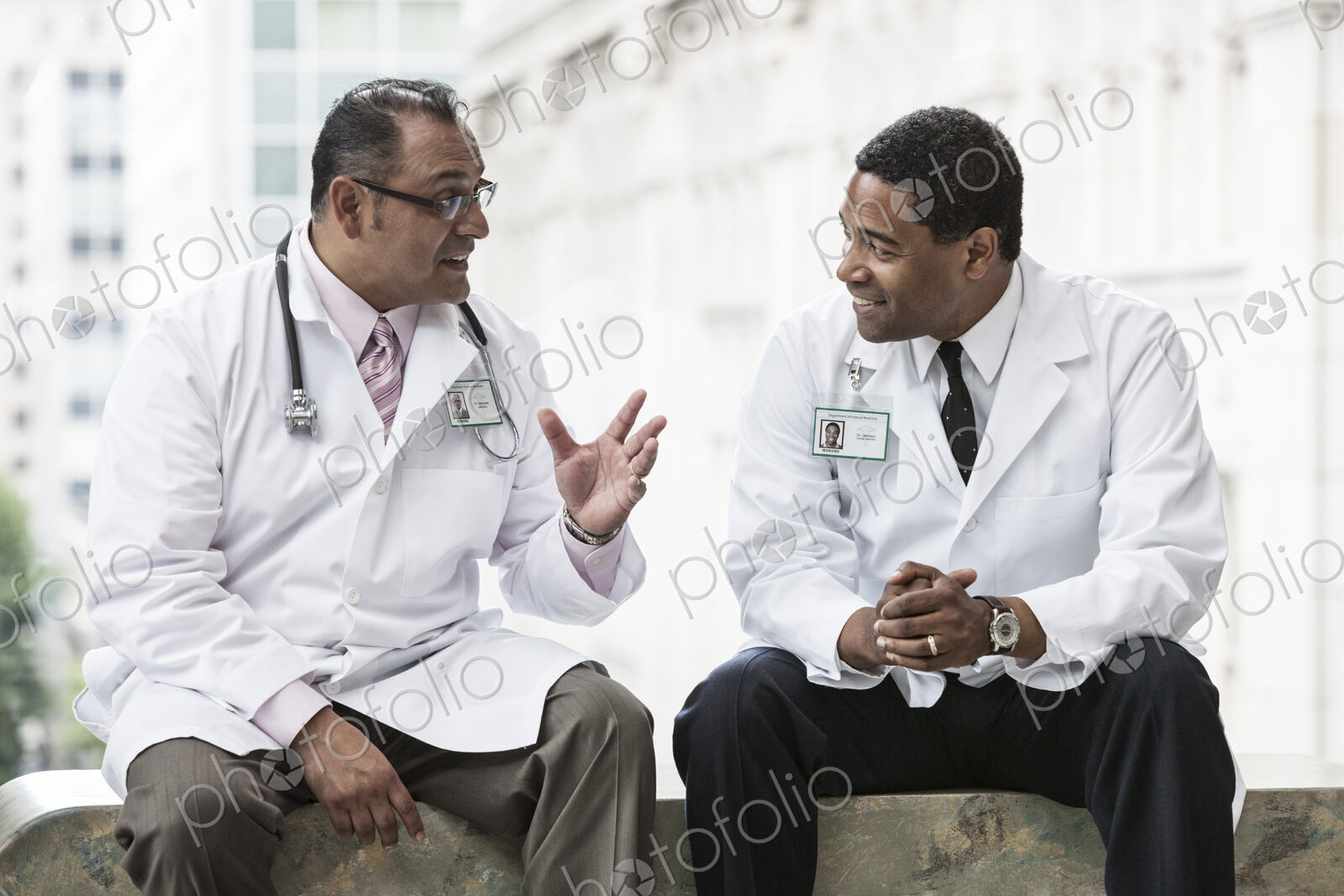 Black and Hispanic male doctors discussing a case in a hospital hallway.