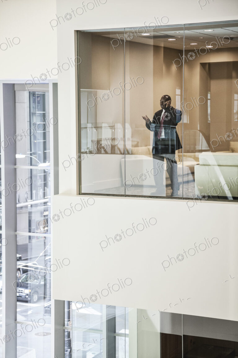 Black busiinessman on the phone standing in a conference room window.