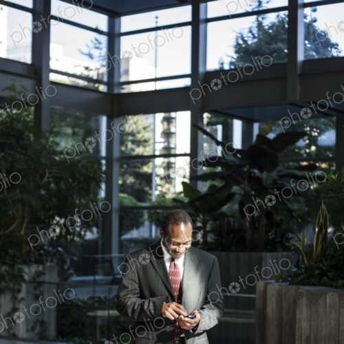 Black busines man texting in a large lobby waiting area. Black busines man texting in a large lobby waiting area.