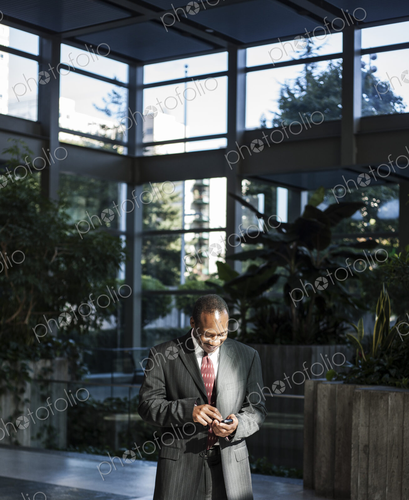 Black business man texting in a large lobby waiting area.