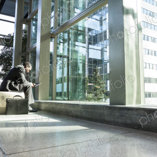 Black business man on a notebook computer sitting in a waiting area of a large open lobby. Black business man on a notebook computer sitting in a waiting area of a large open lobby.