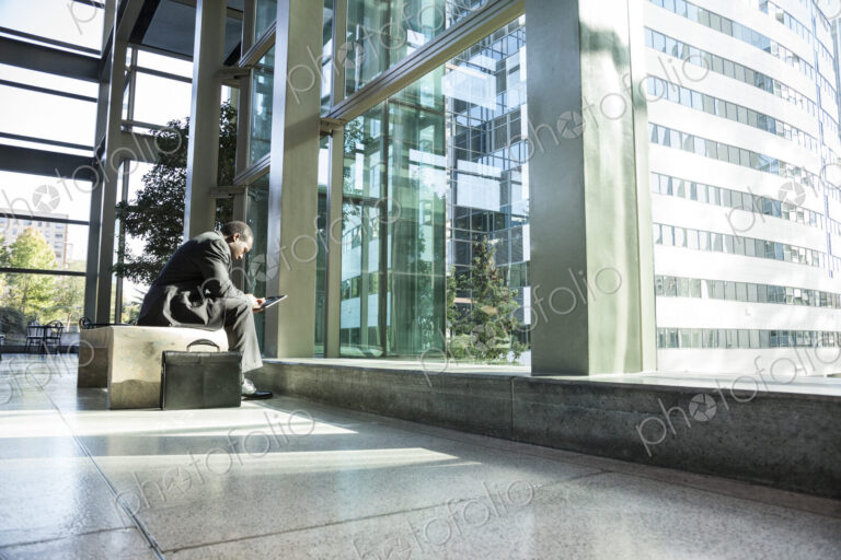 Black business man on a notebook computer sitting in a waiting area of a large open lobby.