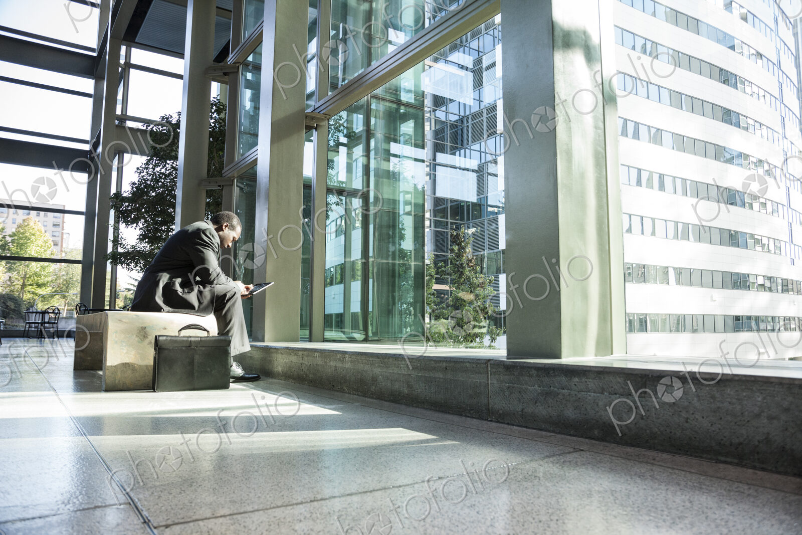 Black business man on a notebook computer sitting in a waiting area of a large open lobby.