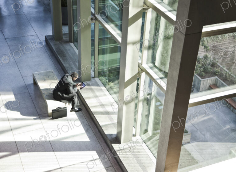 Black business man on a notebook computer sitting in a waiting area of a large open lobby.