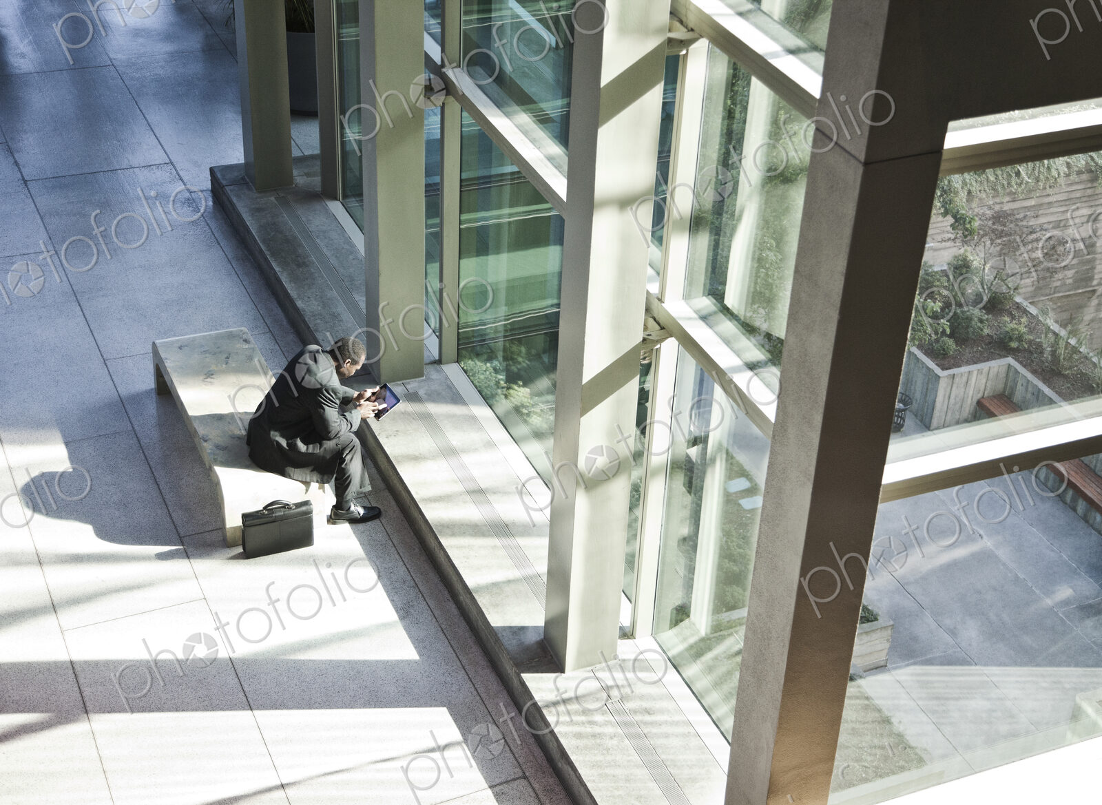Black business man on a notebook computer sitting in a waiting area of a large open lobby.