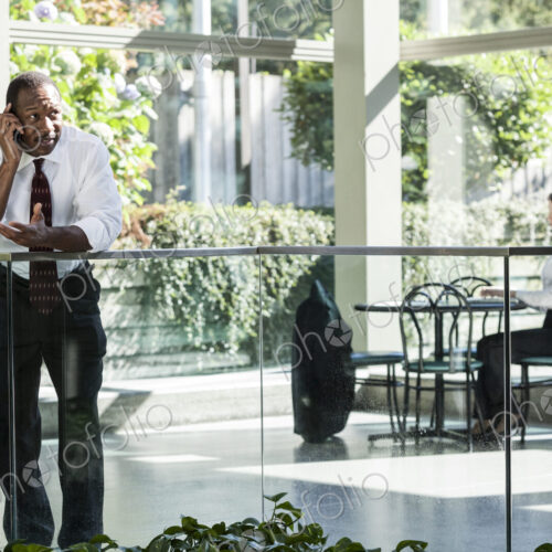 Black business man on the phone in a large open lobby waiting area.