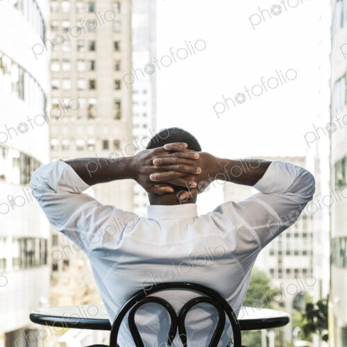 Black business man sitting at a lobby table looking at the cityscape through a large… Black business man sitting at a lobby table looking at the cityscape through a large…