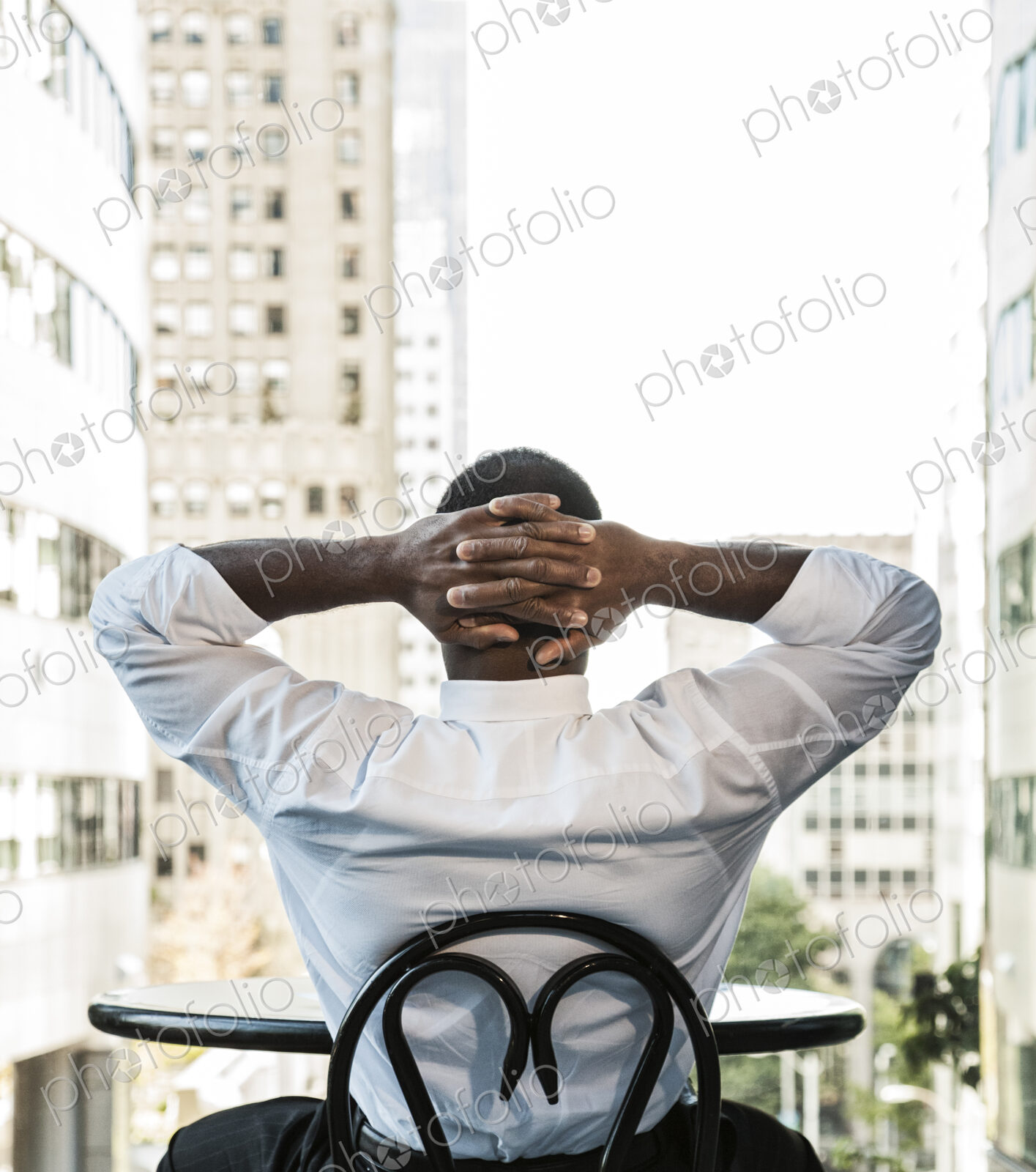 Black business man sitting at a lobby table looking at the cityscape through a large…