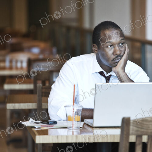 Black business man working on a lap top computer in a coffee shop.