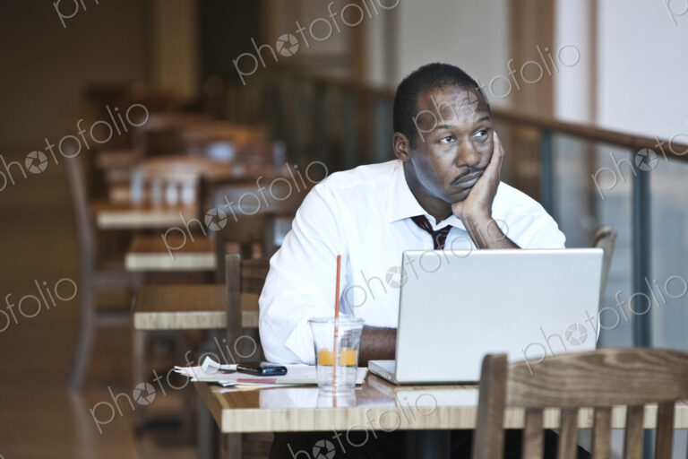 Black business man working on a lap top computer in a coffee shop.