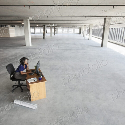 Black business woman sitting at a desk working on a computer in a large new empty…