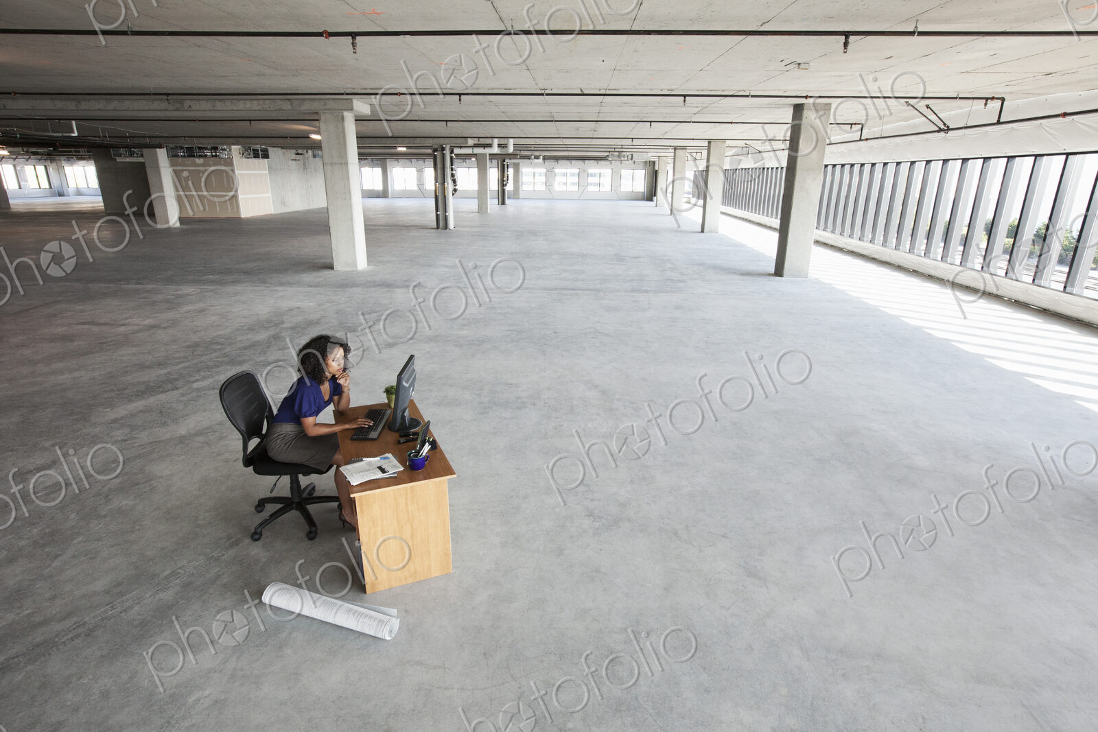 Black business woman sitting at a desk working on a computer in a large new empty…