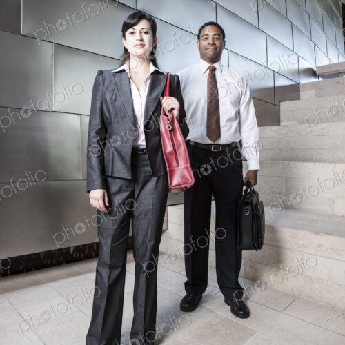Black businessman and Hispanic businesswoman in the lobby of a large office building.