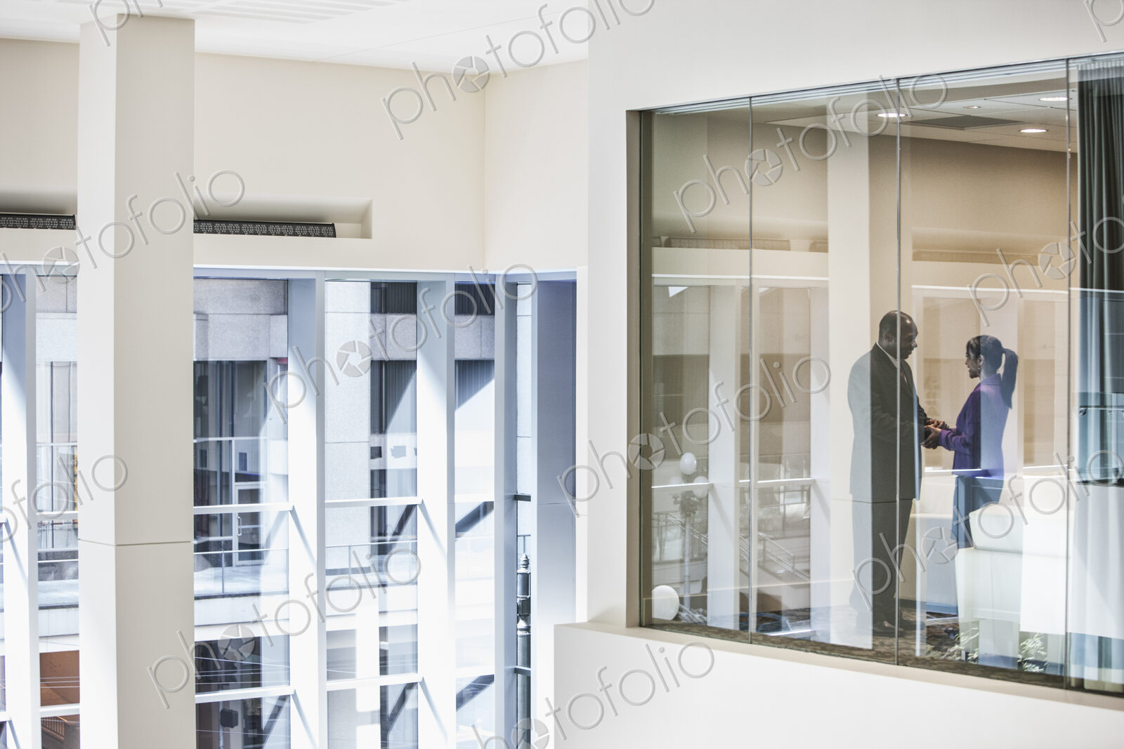 Black businessman and woman shaking hands in conference room window.