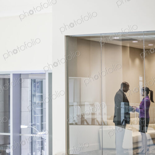 Black businessman and woman shaking hands in conference room window.