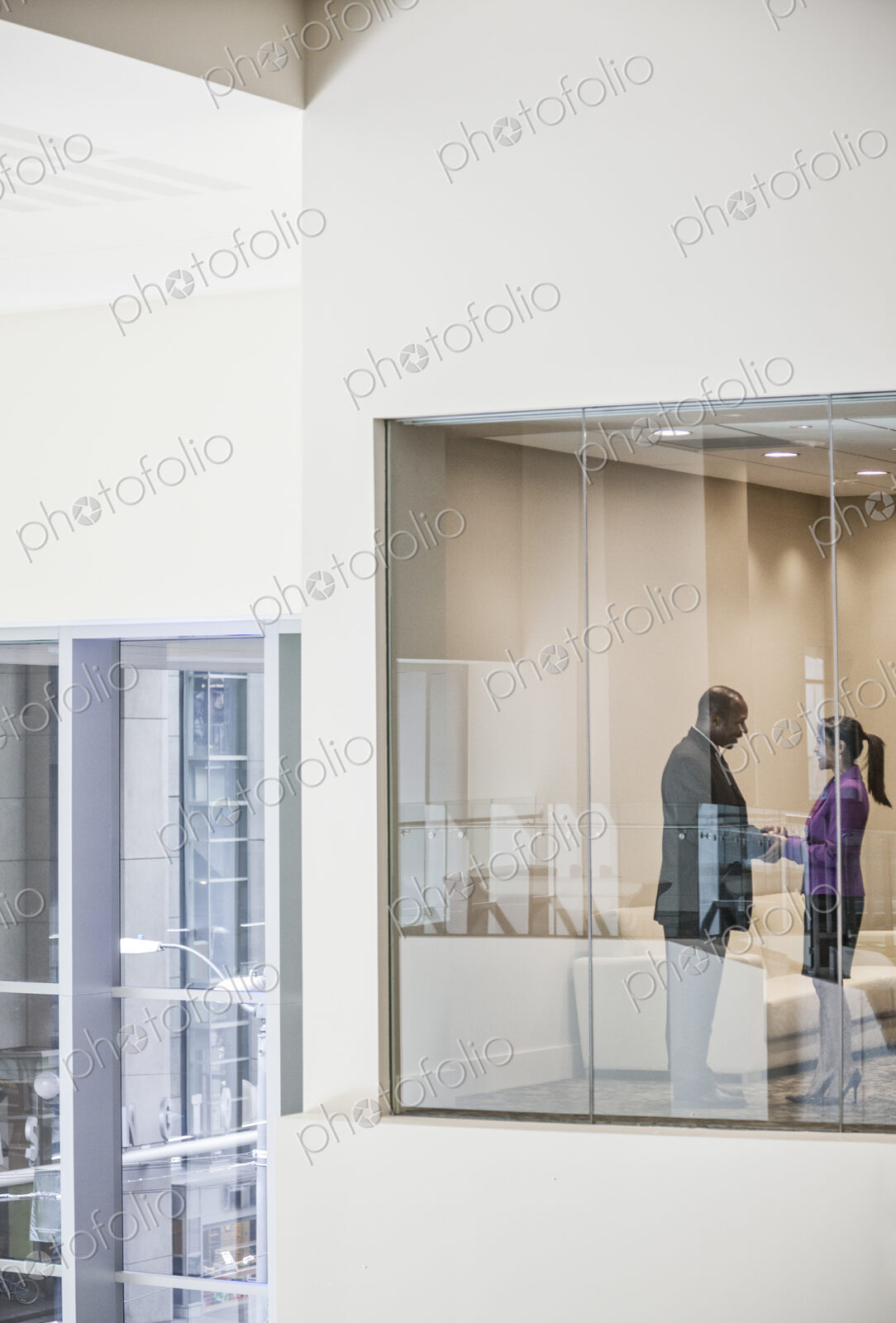 Black businessman and woman shaking hands in conference room window.