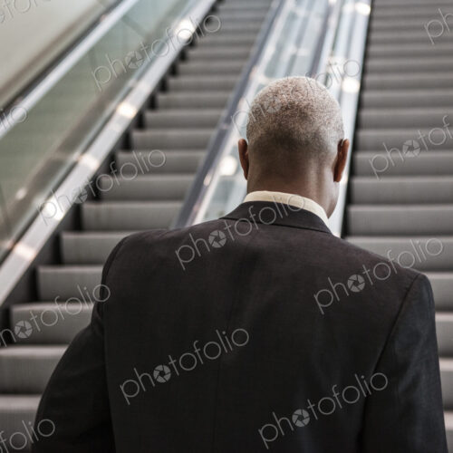 Black businessman on his way up an office escalator.