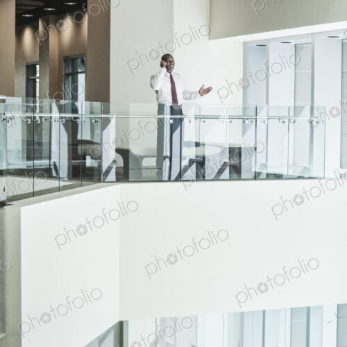 Black businessman on the phone standing in the lobby of a large business center. Black businessman on the phone standing in the lobby of a large business center.