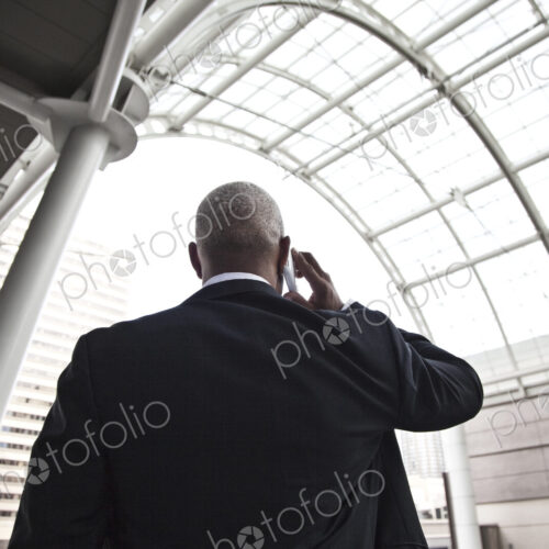 Black businessman on the phone while walking throiugh a large glass covered walkway.