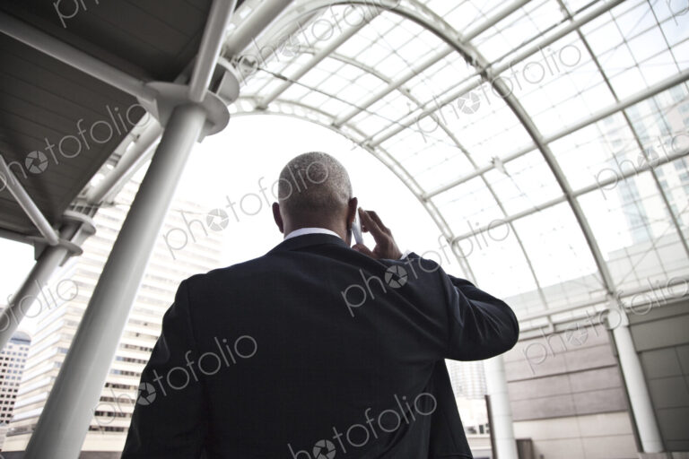Black businessman on the phone while walking throiugh a large glass covered walkway.