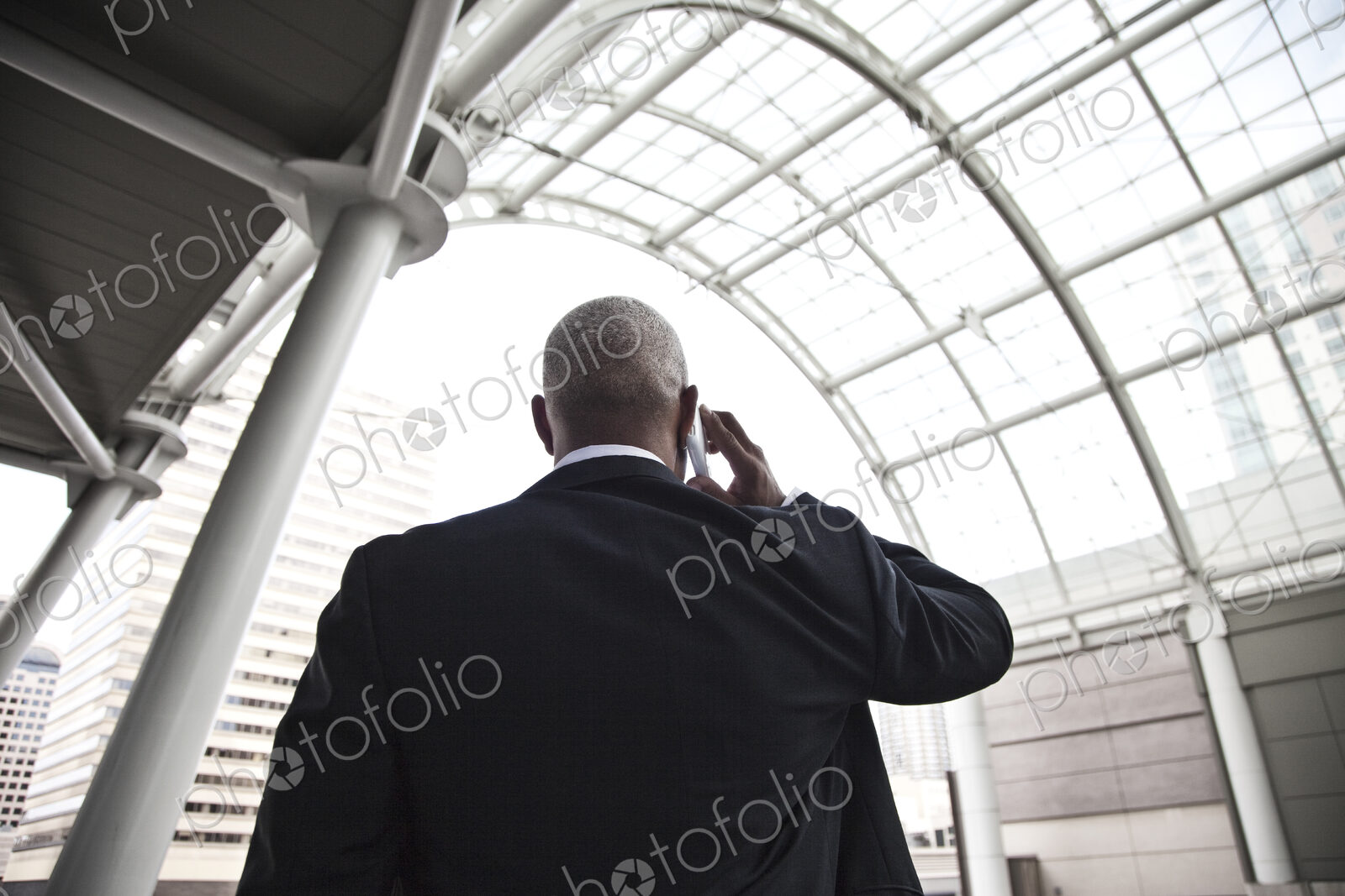 Black businessman on the phone while walking through a large glass covered walkway.