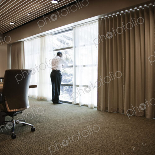 Black businessman standing at a window next to a large conference table. Black businessman standing at a window next to a large conference table.
