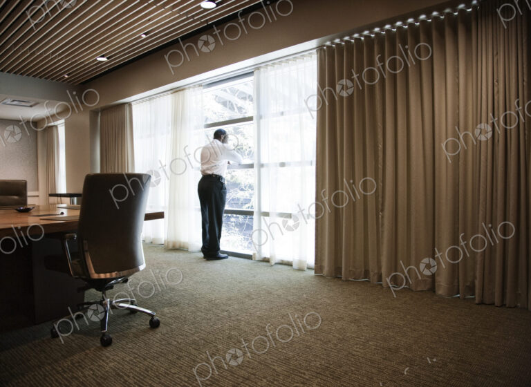 Black businessman standing at a window next to a large conference table.