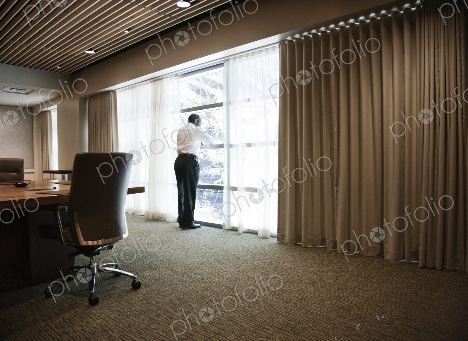 Black businessman standing at a window next to a large conference table.