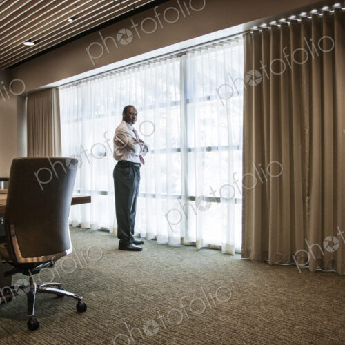 Black businessman standing at a window next to a large conference table. Black businessman standing at a window next to a large conference table.